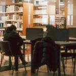 Student in the Library Reading Room Separated by a Glass from the Bookcases